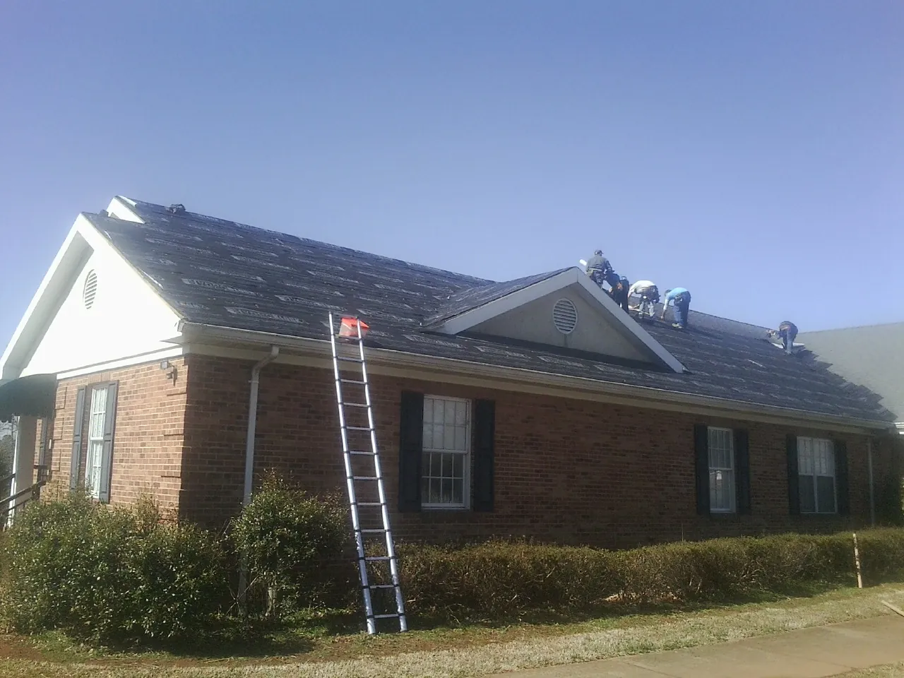 Crew tearing shingles off a brick ranch roof with a ladder set — Metal Roof Repair work by our crew in Prudence Island