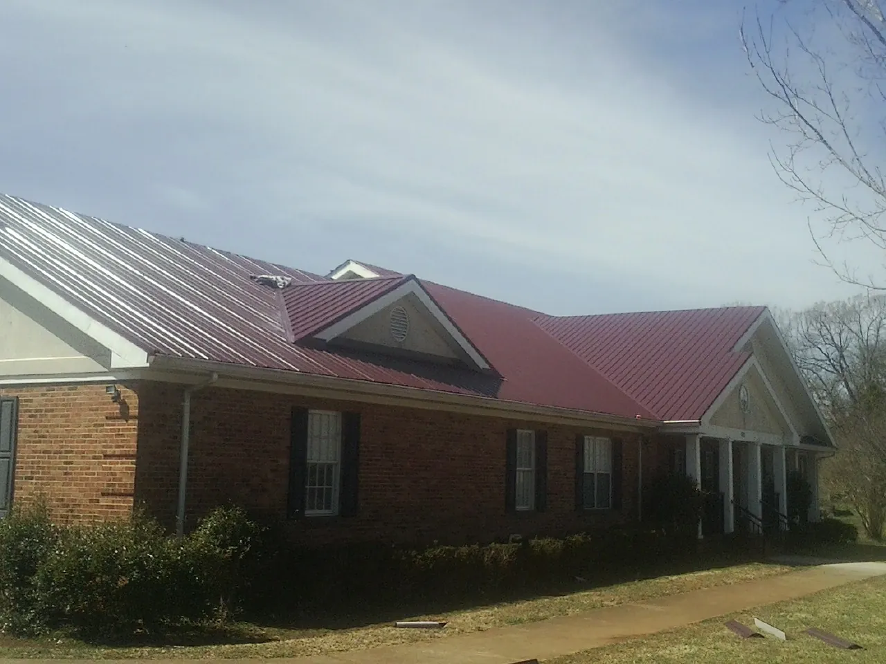 Red metal roof with gabled entries on a long brick building, from a Hail Damage Roof Repair job in Prudence Island