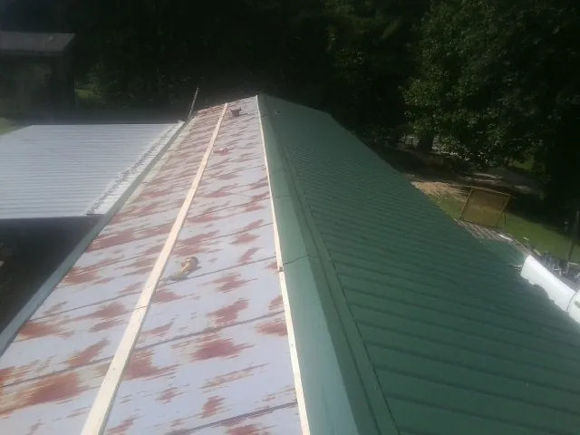Old rusted panels beside newly installed green metal roofing — Wind Damage Roof Repair by Roofing Brothers in Prudence Island