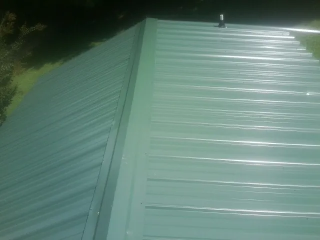 New green metal panels meeting at the ridge of a roof — Flat Roof Repair work by our crew in Prudence Island