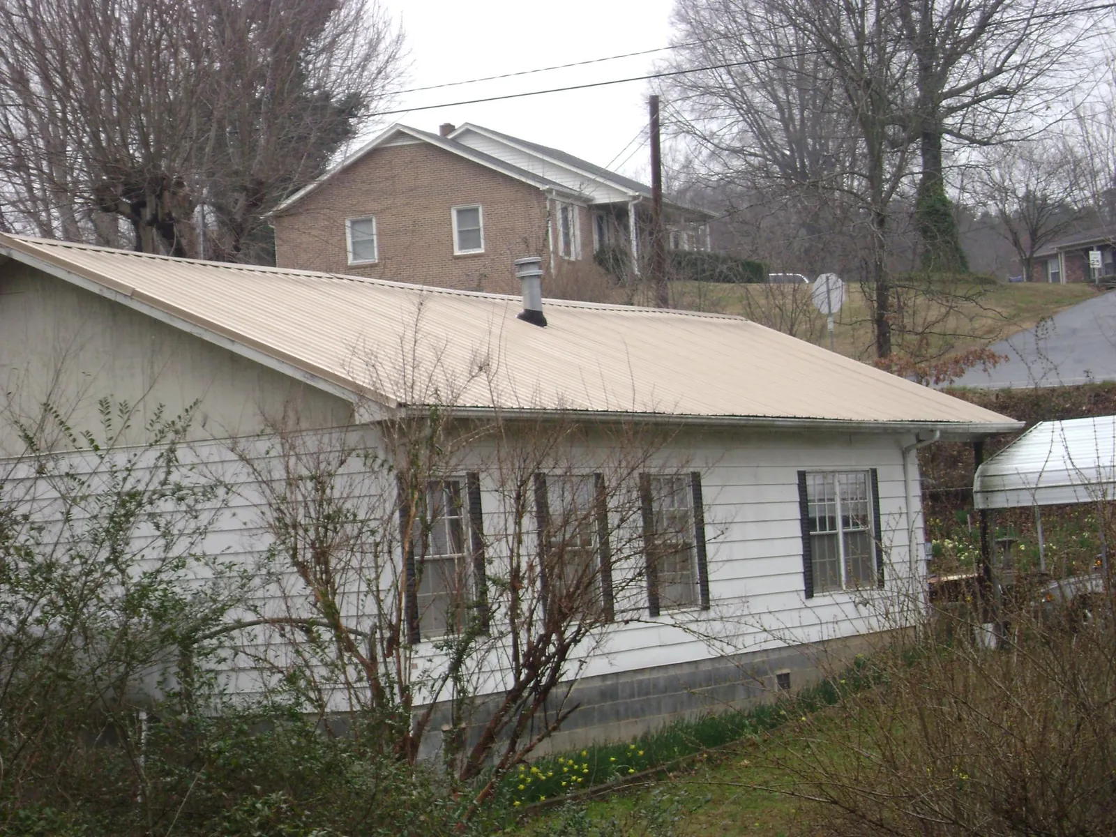 Tan metal roof on a white sided house set into a hillside — Commercial Roofing by Roofing Brothers in Prudence Island